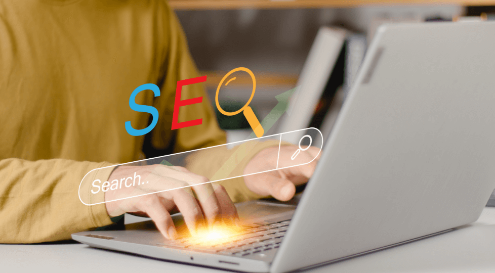 「SEO」の文字と虫眼鏡のアイコン、検索バーが表示されており、キーボードを打っている手元の写真。